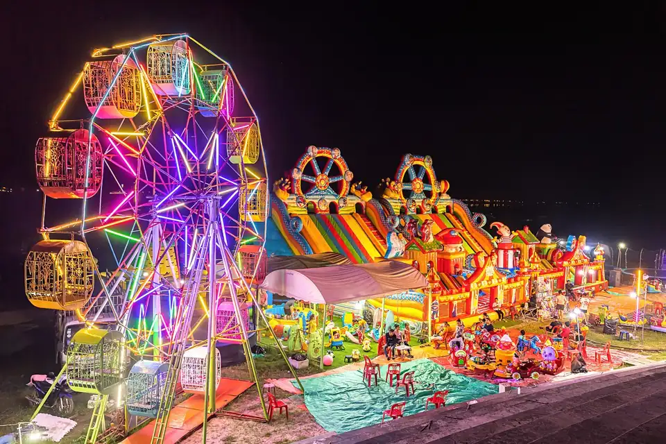 Photo: Illuminated Ferris wheel, bouncing castle and carousel at night in a funfair in Vientiane, Laos